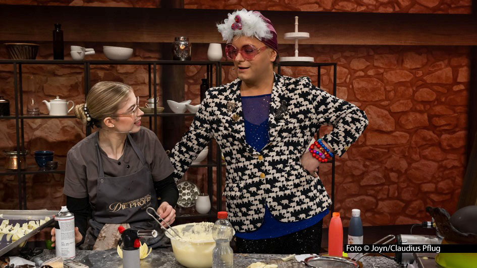 In der zweiten Staffelrunde der Sat.1-Show „Das große Backen – Die Profis“ bekommt das Jury-Trio Christian Hümbs, Bettina Schliephake-Burchardt und Günther Koerffer glamouröse Verstärkung: Entertainer Julian F.M. Stoeckel begutachtet die Schoko-Kopfbedeckung, die die Kandidaten kreieren. Foto © Joyn/Claudius Pflug