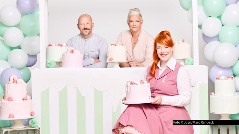 Moderatorin Enie van de Meiklokjes sowie das Jury-Duo Christian Hümbs und Bettina Schliephake-Burchardt sind einmal mehr bereit für eine neue Runde im Sat.1-Wettbewerb „Das große Backen“. Diesmal stehen u.a. Erdbeer-Moussetörtchen und kreativ gestaltete Macarons auf dem Aufgabenplan. (Foto © Joyn/Marc Rehbeck)